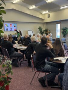 People sit at tables listening to a presentation.