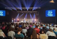 Secure in Jesus Students sitting in chairs looking at stage with band and speaker.