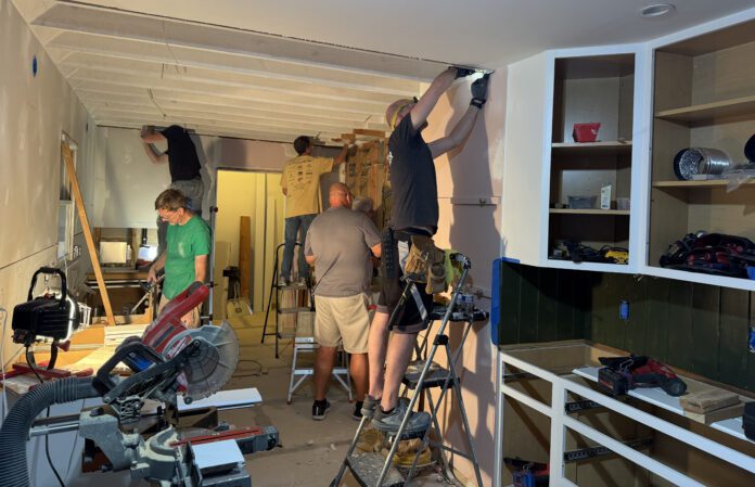 Team of five works on cabinets and kitchen surfaces in construction setting.