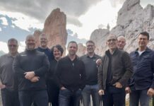 Walking together Eight men and one woman stand before mountainous view.