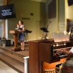 Woman singing at podium while organist plays.
