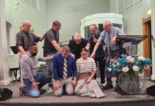 Daniel Rodriguez ordained Man and woman kneel while six people pray over them during a church service.