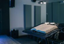 Between sermons Open Bible resting on a black podium inside a modern church hall, with chairs and musical instruments visible in the background.