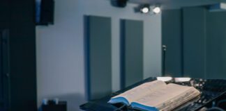 Between sermons Open Bible resting on a black podium inside a modern church hall, with chairs and musical instruments visible in the background.