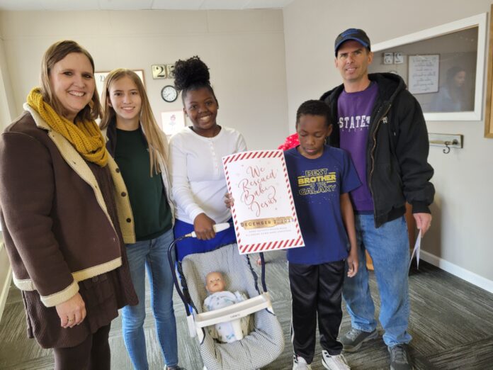 Family stands with toy baby after successfully solving escape room.