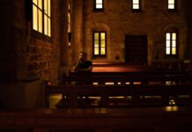 It can be lonely at church Young man is praying sitting on a bench inside of a church. Concept of religion.