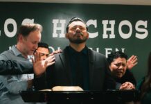 Los Hechos Lincoln Glen starts services with crowded room People praying over couple at front of church.