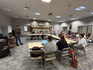 Students at tables listen to lecture.